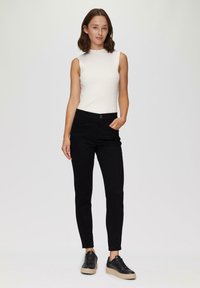 Witte, geribde mouwloze top gecombineerd met zwarte, strakke broek en zwarte sneakers met een gestructureerde zool. Eenvoudig ontwerp, geen opmerkelijke patronen.