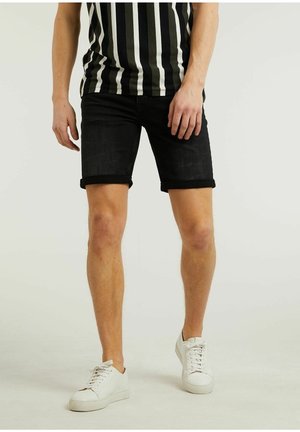Pantalones cortos de mezclilla negros con dobladillos enrollados, combinados con una camisa a rayas en blanco y negro. El modelo lleva zapatillas blancas. Diseño simple y casual.