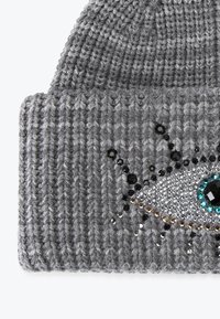 Grijze gebreide muts met ribbelstructuur, voorzien van een decoratief oogontwerp gemaakt van pailletten en kralen in zwart, zilver en turquoise.