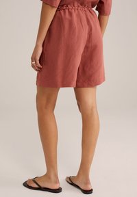 Lněné šortky v barvě rezavě hnědé s elastickým pasem a pleteným detailem, sahající do poloviny stehna, v kombinaci s černými žabičkami.