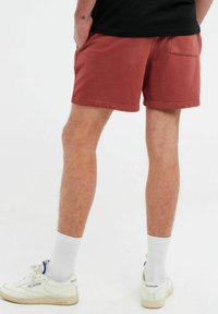 Shorts rossi in cotone con vita elasticizzata, tasche laterali e una tasca sul retro. Indossati con calze bianche e sneakers.