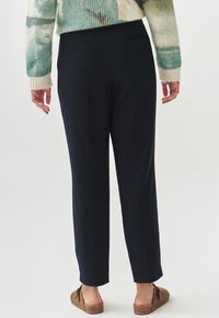 Tmavě námořnické kalhoty se rovnými nohavicemi, měkká tkanina, dvě zadní kapsy a čistý, minimalistický design, nošeny s hnědými nazouvacími botami.