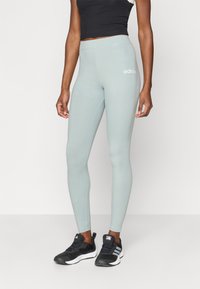 Svetlozeleni legingi izdelani iz raztegljive tkanine z visokim pasom; na levi strani imajo bel logotip Adidas.