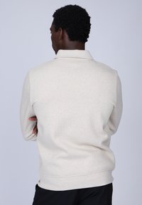 Pull léger gris clair avec une texture subtile, manches longues et col. Présente une coupe décontractée ainsi que des poignets et un ourlet côtelés.