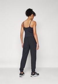 Črn fitted top s tank rameni, v kombinaciji z ohlapnimi črnimi jogger hlačami z elastičnimi manšetami. Model nosi črne športne čevlje.