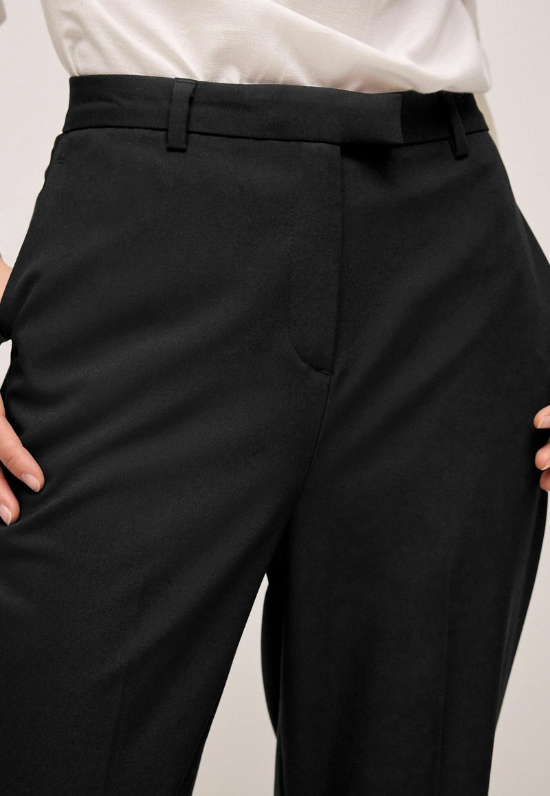 Pantalons noirs parfaitement taillés avec une texture lisse, une coupe droite, des poches avant et un design minimaliste. Parfaits pour une tenue formelle ou décontractée.