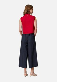 Top rosso senza maniche abbinato a pantaloni ampi blu navy. Il top presenta un piccolo colletto e dettagli sulla schiena; i pantaloni hanno una vestibilità morbida e tasche.