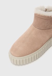Bottine en cuir suedé rose clair avec une semelle en caoutchouc couleur crème et un intérieur en peluche. Présente un bout arrondi et des détails de couture minimalistes.
