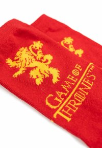 Red socks featuring a yellow lion emblem and the text "GAME OF THRONES." Made from a soft fabric with a knit texture.