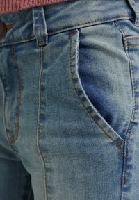 Ljusblå denimjeans med kontrasterande sömmar, en framficka och tapered passform, som framhäver subtil textur och blekning.