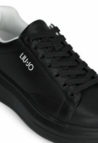 Sneaker in pelle nera con lacci sul davanti, superficie texture e accenti bianchi. Presenta una suola spessa e un logo sul lato.