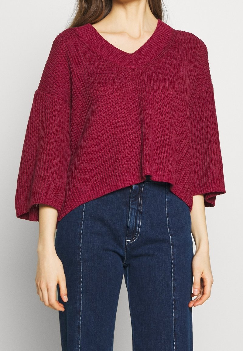 Pull en maille bordeaux oversize avec col en V, manches larges et longueur raccourcie, doté d'une texture côtelée et d'un ourlet droit.