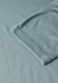 Světle modré bavlněné tričko s hladkou texturou, klasickým kulatým výstřihem a krátkým rukávem. Viditelné švy podél lemu.