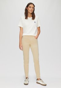 Biała bawełniana koszulka z małym niebieskim serduszkiem. Beżowe spodnie slim-fit oraz sneakersy w dwóch kolorach z teksturowaną podeszwą dopełniają strój.