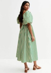 Vestido midi a rayas verdes y blancas con mangas abullonadas y corsé fruncido, combinado con sandalias de tacón color marrón.