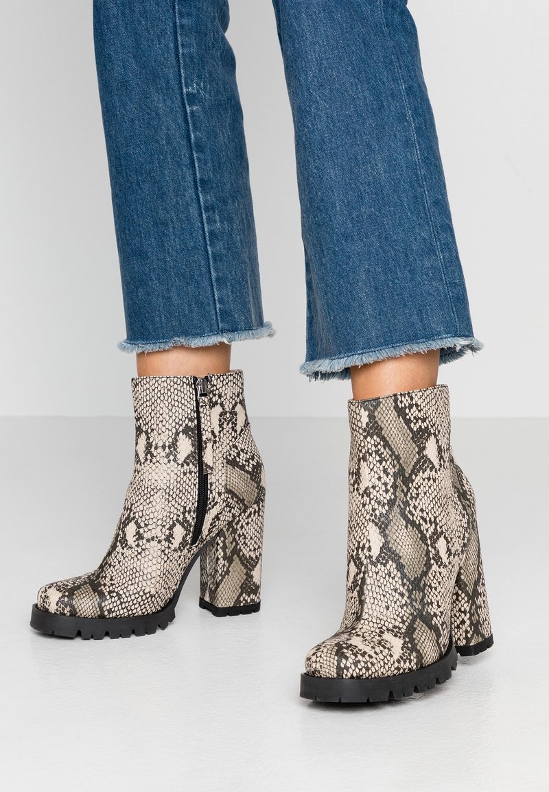 Bottines hauteur cheville imprimé serpent avec talons épais, portées avec un jean bleu court aux bords effilochés.