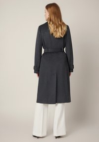 Szary wełniany płaszcz trench z paskiem w talii, zapięty na guziki mankiety i rozporem z tyłu. W połączeniu z białymi spodniami o szerokich nogawkach. Prosty i elegancki design.