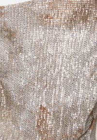 Silberner Paillettenstoff mit glatter Textur, der Licht reflektiert. Die Oberfläche zeigt verstreute Pailletten, die einen schimmernden Effekt erzeugen.