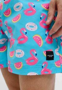 Costume da bagno blu con un motivo colorato di fenicotteri rosa, ciambelle e fette di anguria. Include un'etichetta nera con "JACK & JONES."