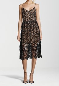 Robe noire en dentelle avec un corsage ajusté, des bretelles fines et une jupe à volants transparente. Présente des motifs floraux complexes et un ourlet festonné.