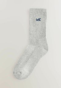 Sivé rebrované ponožky s jemnou textúrou, s vyšitým slovom "self" v námorníckej modrej farbe. Dizajn zahŕňa štandardný tvar a dĺžku ponožiek.
