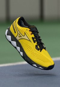 Chaussure de sport jaune avec un dessus texturé, des accents noirs et une semelle épaisse blanche et grise, dotée d'un design élégant et aérodynamique.