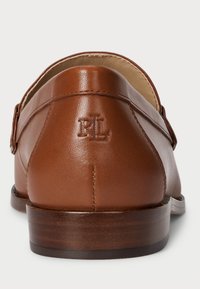 Καφέ δερμάτινες loafers με λεία υφή, διαθέτοντας χαμηλό τακούνι και διακριτική ανάγλυφη λεπτομέρεια λογότυπου στο τακούνι. Στρογγυλή σχεδίαση πίσω.