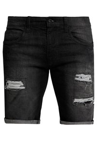 Shorts en denim noir avec des revers retroussés, présentant des patches usés sur la cuisse gauche et deux sur la cuisse droite.