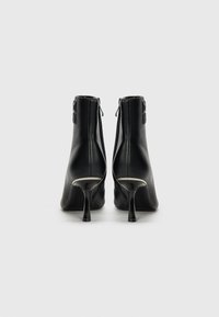 Bottines en cuir noir avec une finition texturée, talons hauts effilés et boucles décoratives à la cheville. Fermeture éclair à l'arrière.