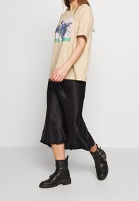 Beige bomull t-shirt med blommönster, tillsammans med en svart satäng-långkjol. Stilen kompletteras med svarta ankelboots med metallaccenter.