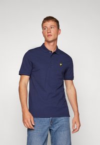Polo shirt bleu marine en coton, à manches courtes, avec trois boutons au col, présentant un petit logo jaune sur la poitrine. Coupe décontractée.