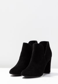 Botas de tobillo de ante negro con punta afilada, lados abiertos y tacón grueso. Textura suave sin patrones visibles ni herrajes.