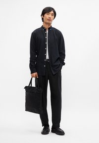 Cămașă albastră închis cu mânecă lungă și guler, asortată cu pantaloni negri și o geantă din țesătură neagră. Textură netedă și detalii cu nasturi.