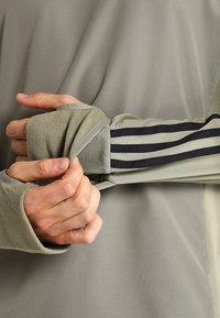Graues sportliches Langarmshirt mit strukturierter Oberfläche, featuring einen Fleecebund und drei dunklen Streifen entlang des Ärmels.