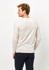 Beige Langarmshirt aus weichem Stoff mit lässiger Passform und rundem Ausschnitt, kombiniert mit dunkelblauen Hosen.