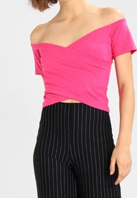 Top ajustado, sin mangas, en rosa brillante, con un diseño de envoltura. Combinado con pantalones de tiro alto a rayas verticales en negro. Textura de tela suave.