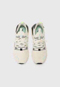 Lightweight cream sneakers with black stripes, aqua accents, and a textured mesh upper. Features flat laces and black heel cap.
