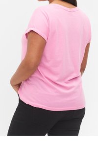 Rosa kortærmet t-shirt lavet af blød bomuld, med en afslappet pasform og opkrøllede ærmer, parret med sorte jeans. Bagview vist.
