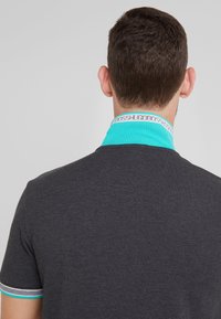 Mörkgrå polo skjorta med en turkos krage och manschetter. Har en subtilt strukturerad tyg och en märkesspecifik detalj på den inre kragen.