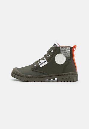 Green high-top boots with rubber sole and fabric upper. Features include white logo patches and an orange accent at the heel.