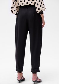 Zwarte, high-waisted broek met een ontspannen pasvorm en opgerolde boorden. Gladde stof met strakke lijnen, gecombineerd met een blouse met stippenpatroon.