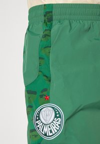 Zelene kratke hlače s kamuflažnim vzorcem, elastičnim pasom, stransko žepom, vezenim logotipom "PALMEIRAS" in rdečo zvezdico.