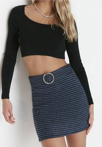 Top corto de manga larga negro con detalles en relieve y escote cuadrado, combinado con una minifalda de patrón de espiga azul y un detalle de anillo plateado en la cintura.