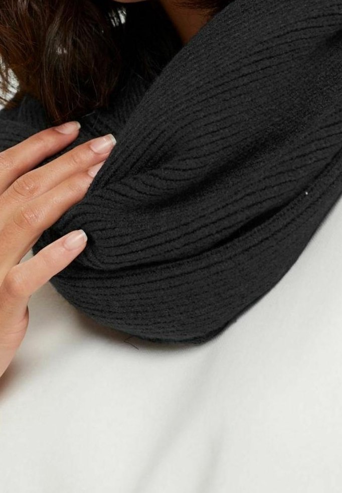 Main avec des ongles naturels touchant un tissu en maille côtelée noire, avec une partie du visage d'une personne et des cheveux foncés visibles au-dessus.