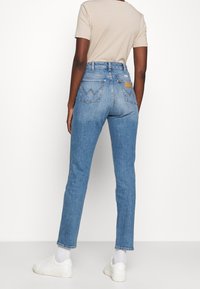 Ljusblå högmidjade jeans med rak passform, med bakfickor och en brun läderlapp. Bärs med vita sneakers.