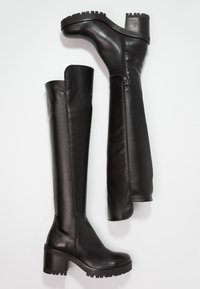 Botas de cuero negras hasta la rodilla con tacón grueso, punta redonda, cremallera lateral y suela de goma texturizada. Acabado liso y elegante.