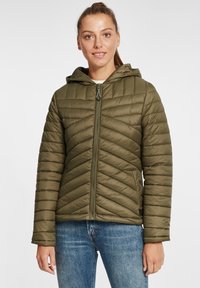 Oliven grønn boblejakke med hette, med chevron-quilting, glidelås foran og en tettsittende design. Brukt over en lys genser.