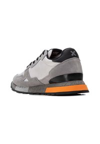 Zapatilla gris y negra con material de ante y reflectante, que presenta una suela texturizada, un acento naranja en el talón y un logotipo distintivo en la parte trasera.