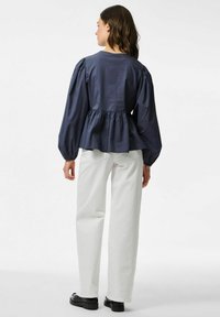 Mörkblå peplum-blus med puffärmar, texturerad bomullstyg och insydd midja. Matchad med vita raka byxor och svarta skor.