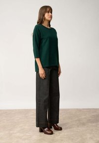 Maglione verde a maglia con maniche a tre quarti, abbinato a pantaloni ampi in denim scuro. Scarpa con tacco blocco marrone completa l'outfit.